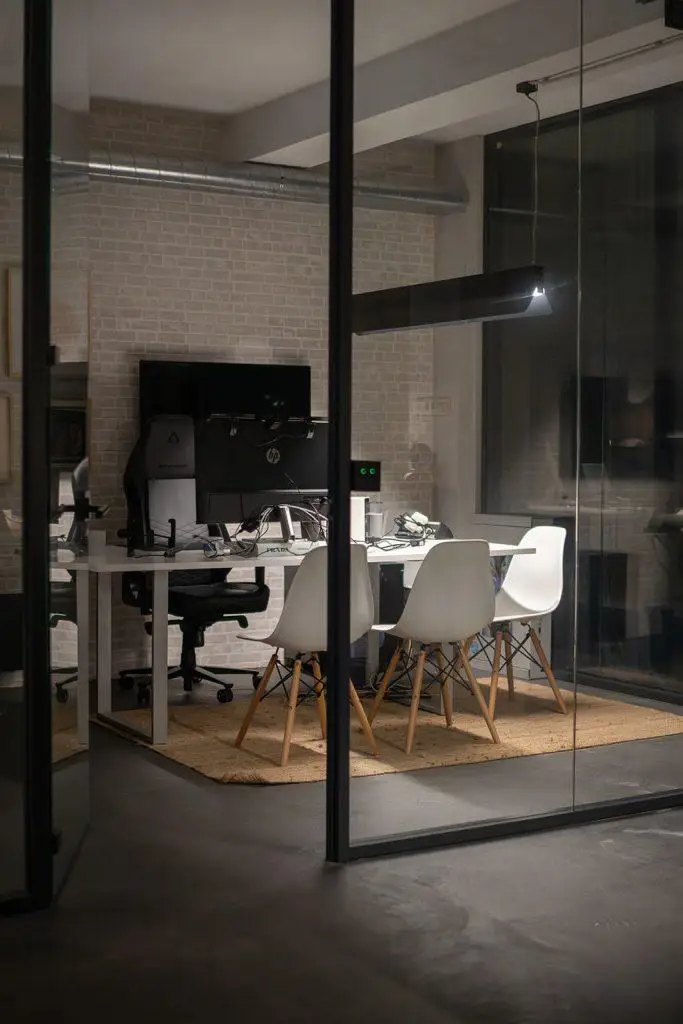 Escritório privado no Outglocal Coworking em Aveiro, com uma estação de trabalho multi-monitor e cadeiras de design brancas.