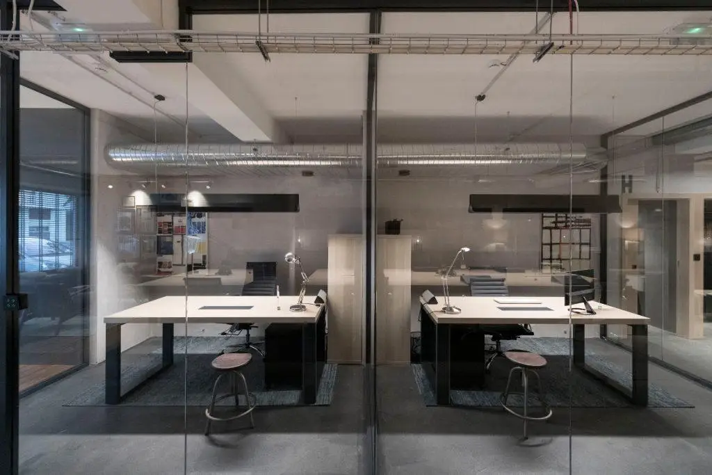 Gabinete de equipa privado no Outglocal Coworking Aveiro, visto através da divisória de vidro, com amplas secretárias de trabalho.