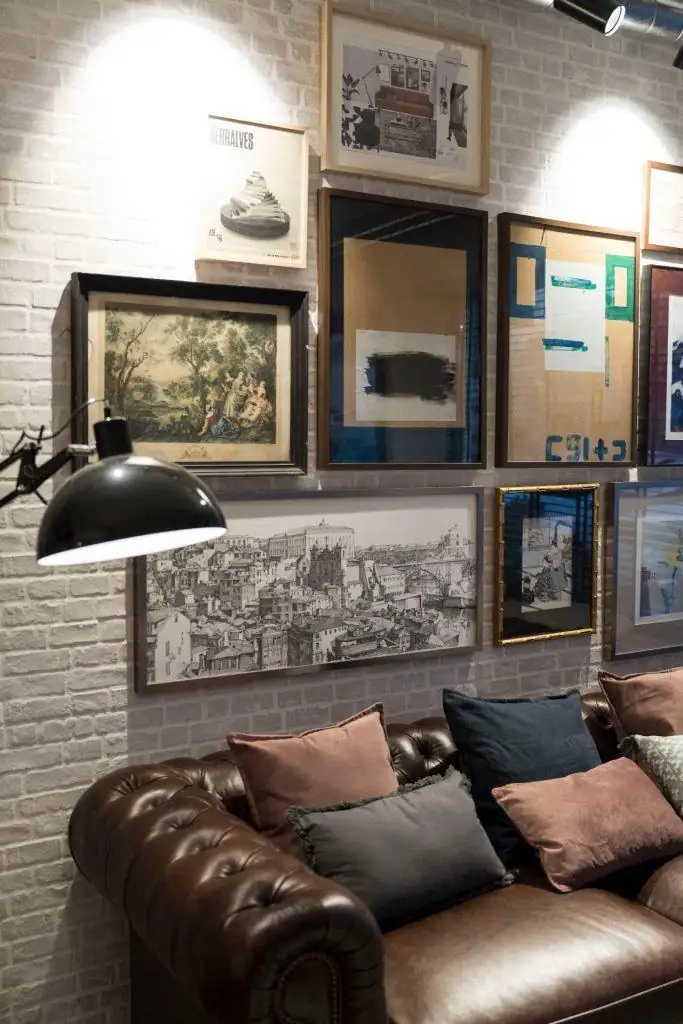Pormenor da área de lounge no Outglocal Coworking Aveiro, com um sofá de cabedal e uma parede de galeria com vários quadros.