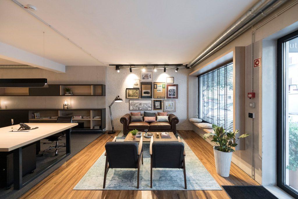 Vista ampla da zona de lounge e open space no Outglocal Coworking Aveiro, com sofá, poltronas e uma estante de trabalho ao fundo.