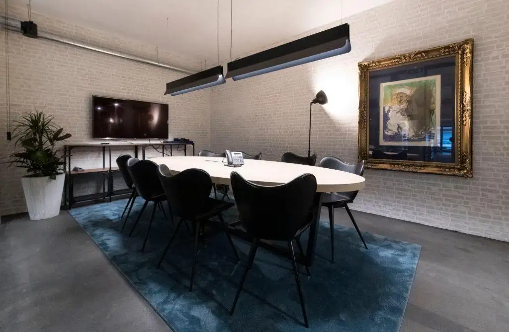 Vista de outra sala de reuniões no Outglocal Coworking Aveiro, com mesa oval, tapete azul e parede de tijolo branco.