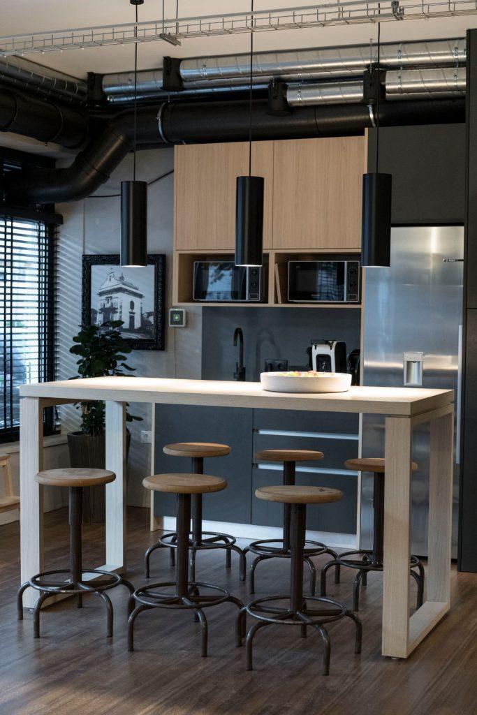 Zona da copa no Outglocal Coworking Aveiro, com uma mesa alta de convívio e uma cozinha equipada ao fundo.